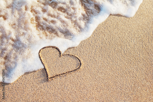 heart symbol handwritten on sandy beach with soft ocean wave