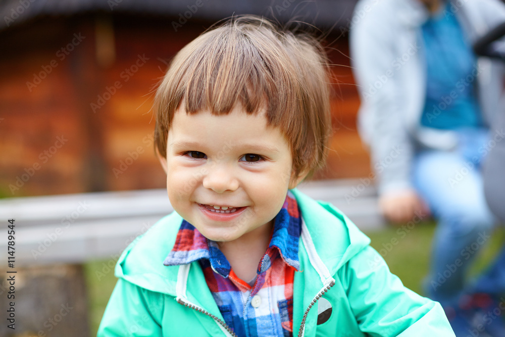 Cute little smiling toddler boy in green jacket and colored checkered shirt playing in summer park, child having fun on fresh green grass. Happy childhood, family weekend, holidays Cute little smiling toddler boy in green jacket and colored checkered shirt playing in summer park, child having fun on fresh green grass. Happy childhood, family weekend, holidays