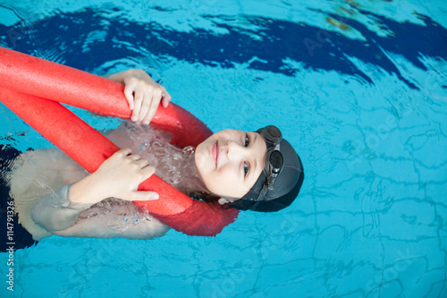 Cute boy swimming with a red foam noodle in a indoor pool