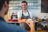 Handsome waiter serving coffee to male customer at cafeteria