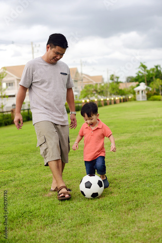 Asian boy play football with his father in the garden 