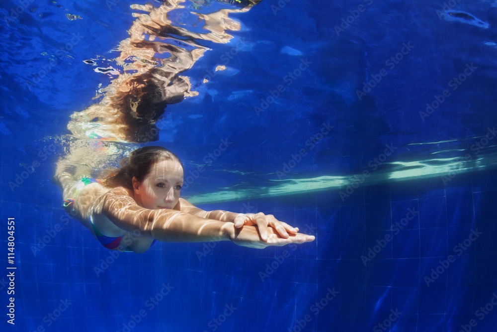 Beautiful young woman dive underwater with fun from poolside to blue pool. Healthy active lifestyle, people water sport activity to keep fit and swimming lessons in health club on summer holidays.