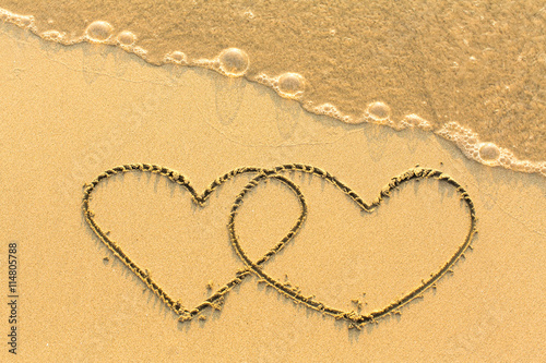 Couple of hearts drawn by hand on a sandy golden sea beach.