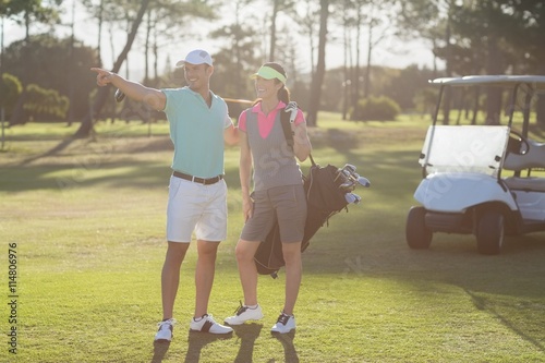 Smiling golf player pointing while standing by woman