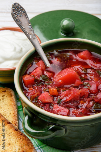 Borscht - traditional russian and ukranian beetroot soup in green ceramic pot on wooden background.