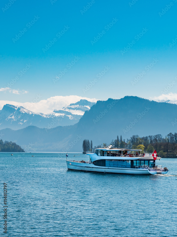 Ferry boat with red swiss flag carry passengers on Lake Lucerne (Vierwaldstattersee) Switzerland. Motor Cruise Ship Waldstatter sail from Weggis full of tourist people under clear blue sky in summer