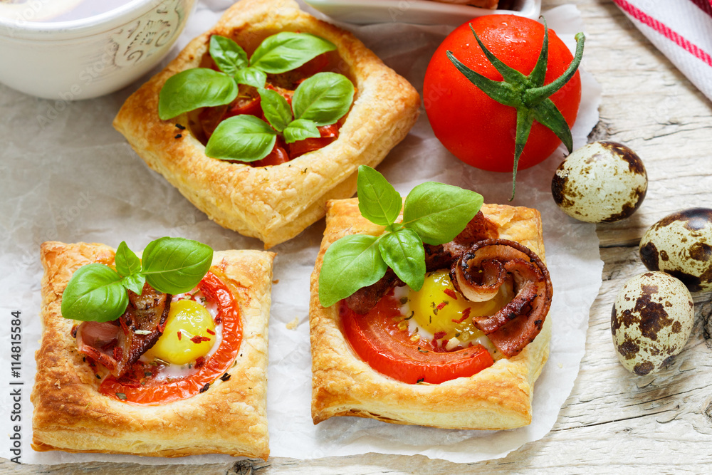 Open pies of puff pastry with quail egg, tomatoes, bacon and Basil. Breakfast. Selective focus
