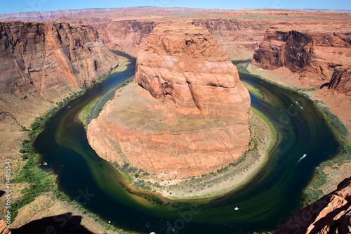 Small boats navigate the Colorado River as seen from approximately 1000 feet above on the rim of Horseshoe Bend, near Page, Arizona, USA.