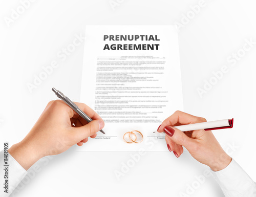 Man and woman sign prenuptial agreement near gold rings. Legal prenup document contract signing by newlywed couple. Marry partners signature on prenupt statement. Wedding ceremony conflict text.

 photo