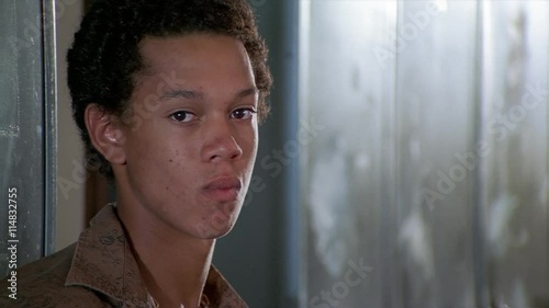 Portrait of an unsmiling curly-haired teenage boy standing near school lockers