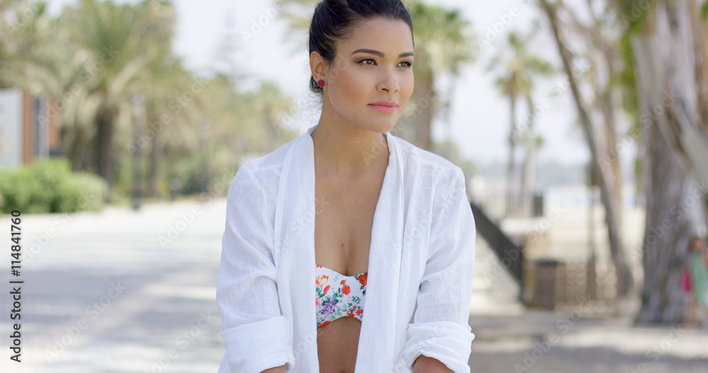 Single young adult woman with calm expression and hand on side of face in white robe while sitting outdoors