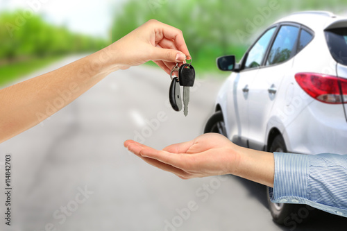 Male and female hands with keys and dollar banknotes on blurred modern car background