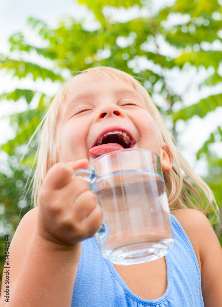 Blonde little girl wearing blue dress holding cup of fresh water with her eyes closed in a summer garden Blonde little girl wearing blue dress holding cup of fresh water with her eyes closed in a summer garden