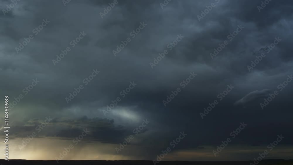 Heavy gray clouds flow across prairie as rain falls along dark horizon, time lapse