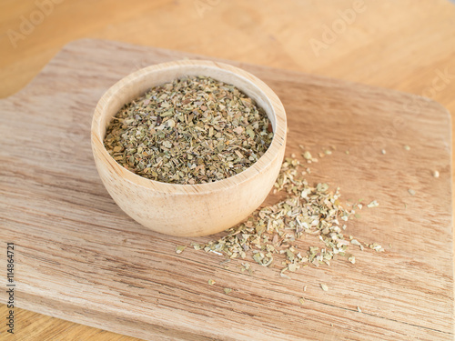 Dried oregano leaves in wooden bowl on chopping board