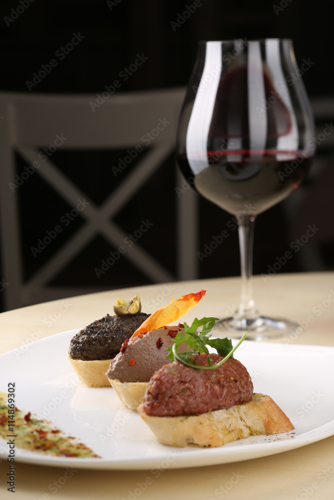 Assortment of pate canapes bread on white plate with glass red wine, dark background