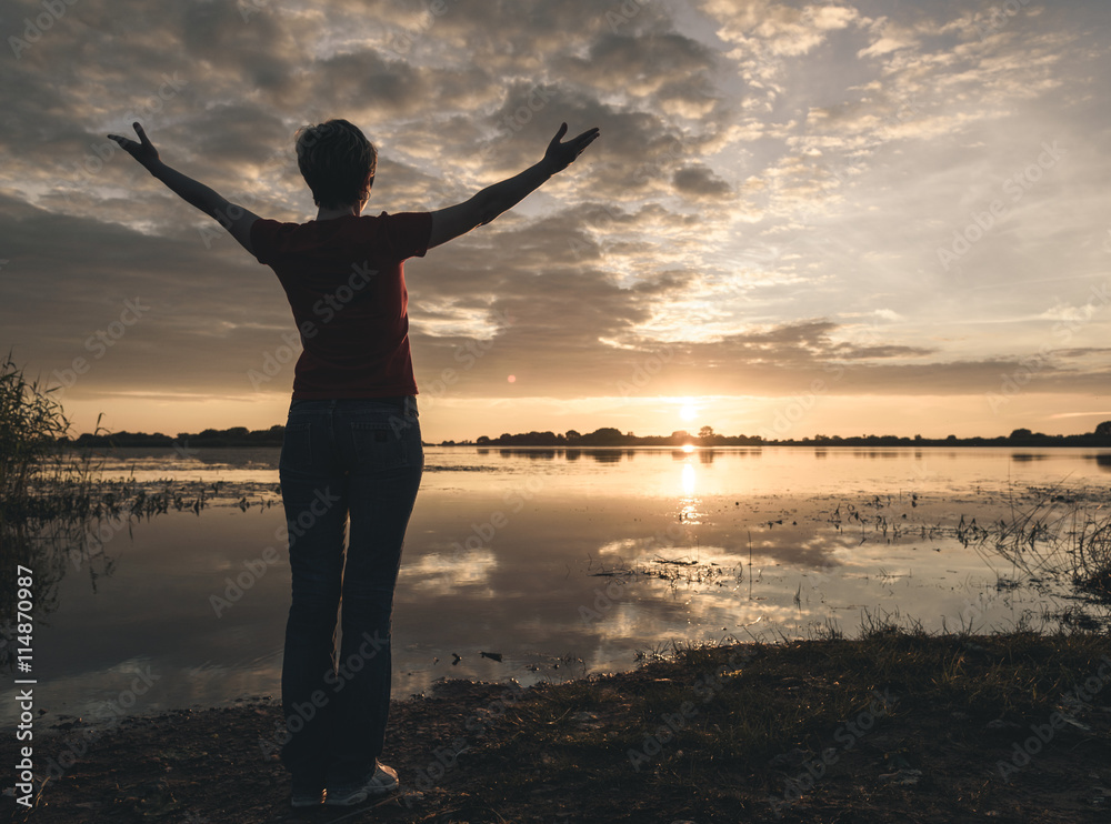 Fototapeta premium young slim woman meditating onbanks of the lake at sunset