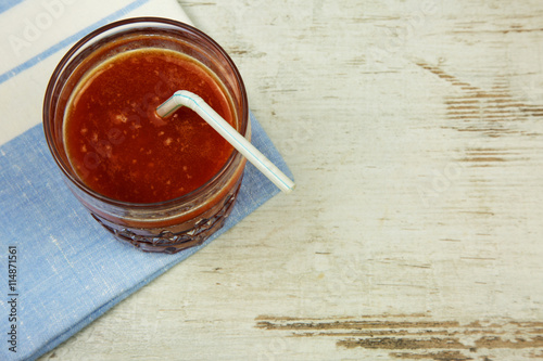 A glass of fresh tomato juice with a straw on a napkin and an ol