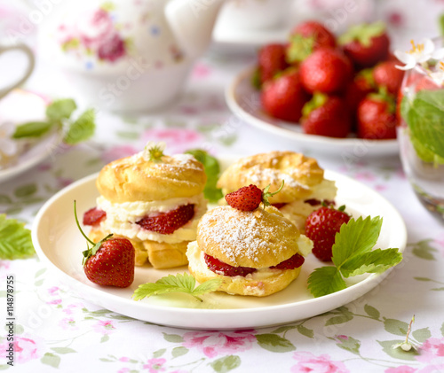 Cream puffs or profiterole filled with whipped cream, powdered sugar topping served with strawberries on the table