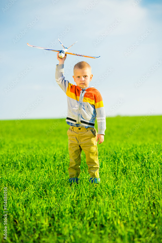 Happy kid playing with toy airplane against blue summer sky background. Boy throw foam plane in green field. Best childhood concept. Happy kid playing with toy airplane against blue summer sky background. Boy throw foam plane in green field. Best childhood concept.