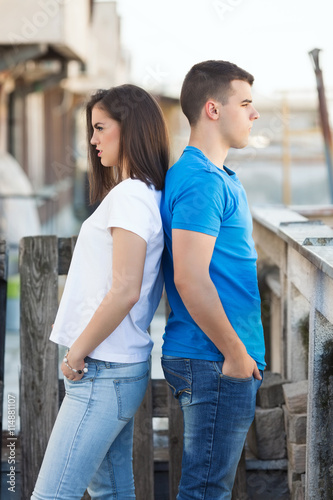 Portrait of teenage couple. Young woman and man are standing back to back and looking away.