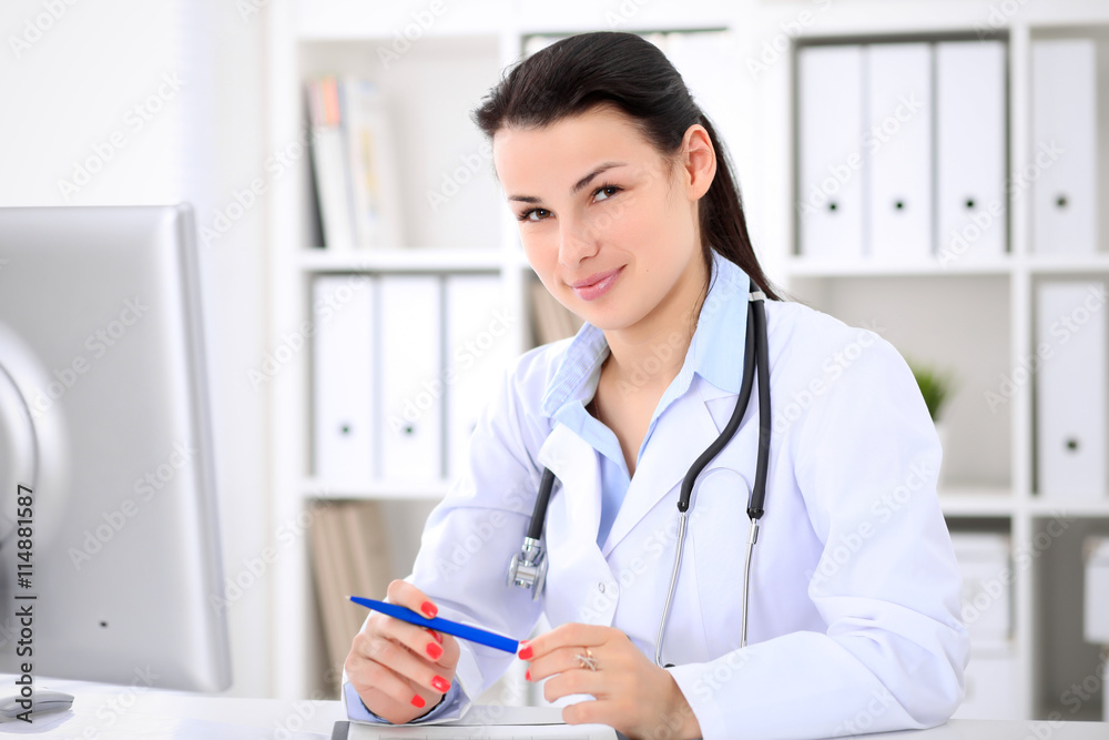 Young brunette female doctor sitting at the table and working by computer at hospital office. Doctor is in trouble with diagnosis. Health care, insurance and help concept. Young brunette female doctor sitting at the table and working by computer at hospital office. Doctor is in trouble with diagnosis. Health care, insurance and help concept.