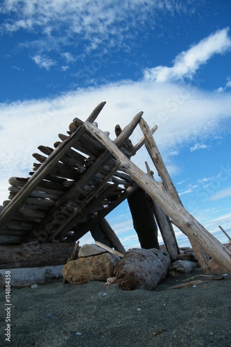 Driftwood Shelter on a Sandy Beach with Clouded Blue Sky