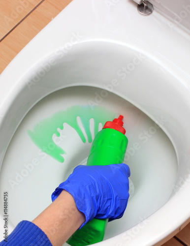 Hand of woman in blue glove cleaning toilet bowl