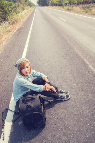 Rear view of a young woman hitchhiking carrying backpack sitting