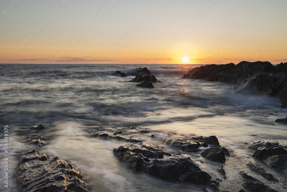 Obraz premium Beautiful vibrant sunset landscape image of calm sea against roc