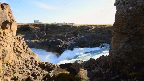 Waterfall with heavy flow and spray, with houses in background