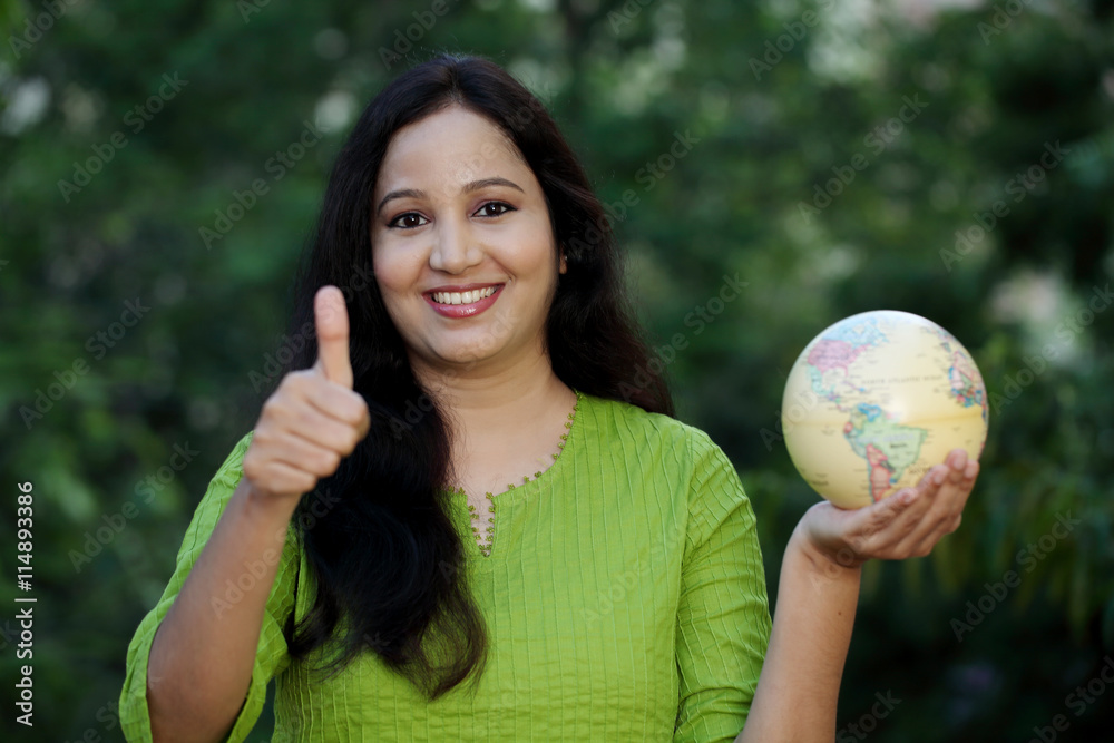 Young woman holding globe and making thumb up gesture Young woman holding globe and making thumb up gesture