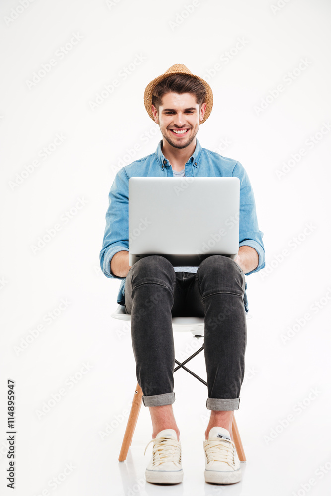 Smiling man in hat sitting on chair and using laptop Smiling man in hat sitting on chair and using laptop