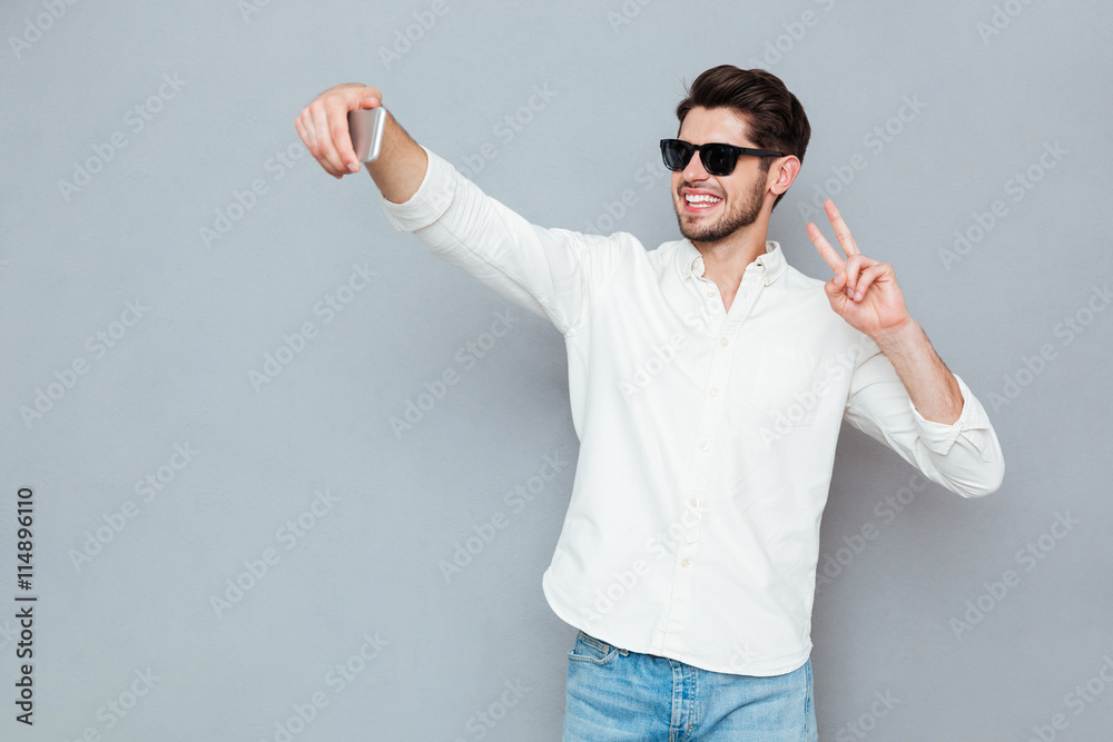 Happy man making selfie photo on smartphone over gray background Happy man making selfie photo on smartphone over gray background