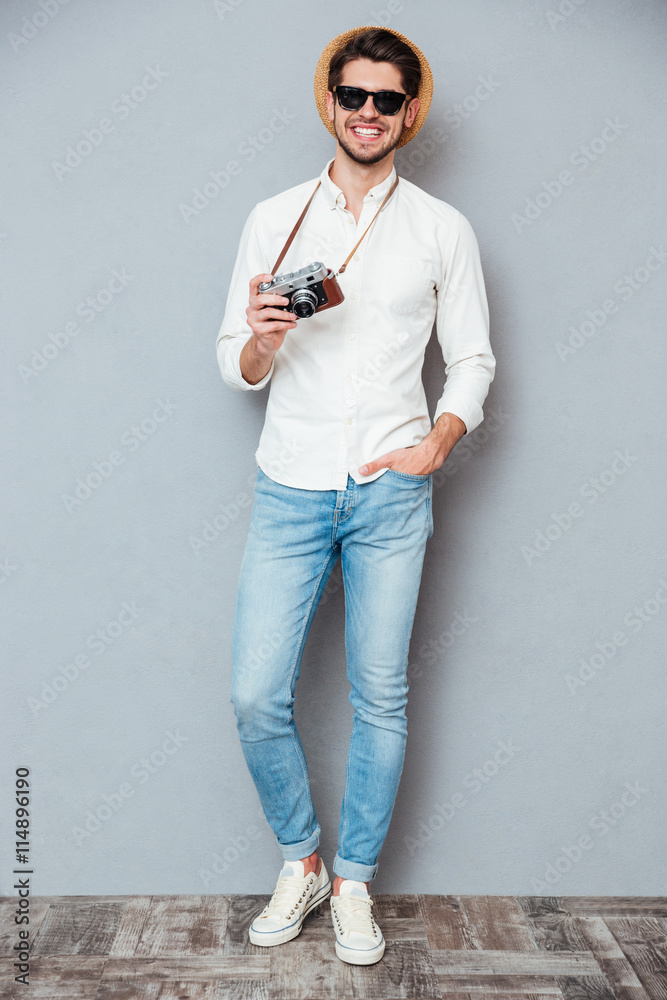 Happy young man in sunglasses standing and holding vintage camera