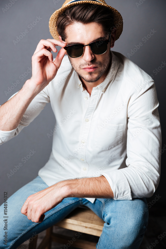 Serious young man in white shirt, jeans, sunglasses and hat Serious young man in white shirt, jeans, sunglasses and hat