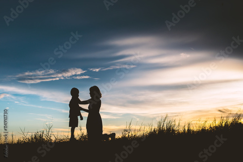 Mother encouraged her son outdoors at sunset, silhouette concept © Johnstocker