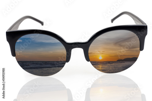 Sunset on the beach reflected where the lenses in black sunglass