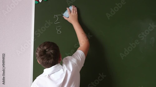 Teenager schoolboy wipes a blackboard to solve the example. photo