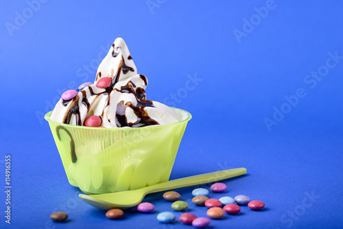 frozen yogurt with chocolate and chocolate candy topping on blue background with green spoon and chocolate candy