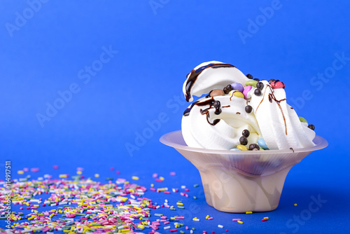 frozen yogurt with chocolate and chocolate candy topping on blue background with rainbow sprinkles