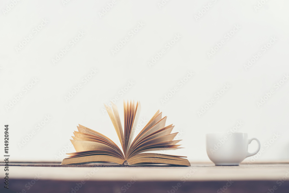 Naklejka premium Vintage old book with coffee cup on wooden deck table background