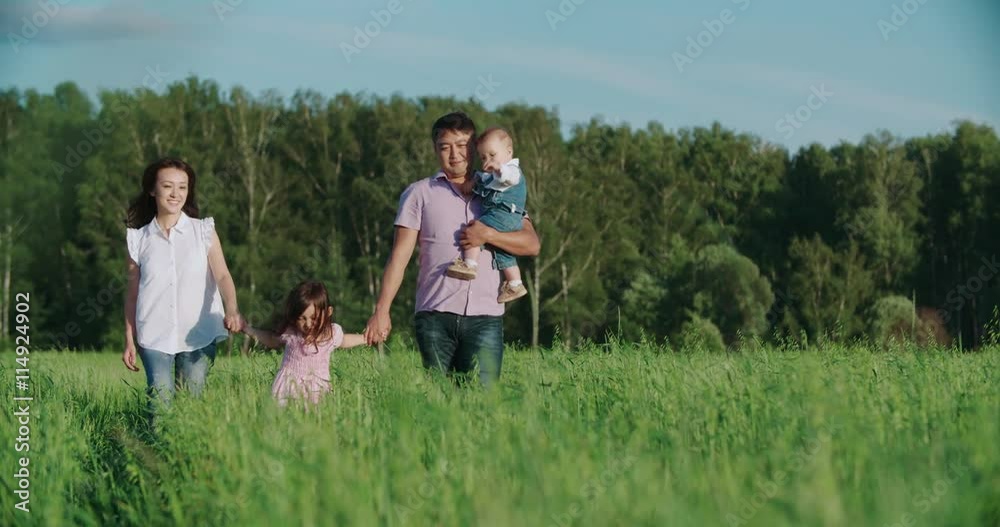 young happy Asian family goes on a green field with two children, slow motion young happy Asian family goes on a green field with two children, slow motion
