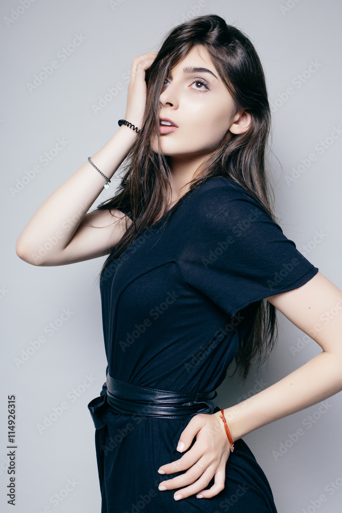 Young brunette lady in black dress posing on grey background Young brunette lady in black dress posing on grey background