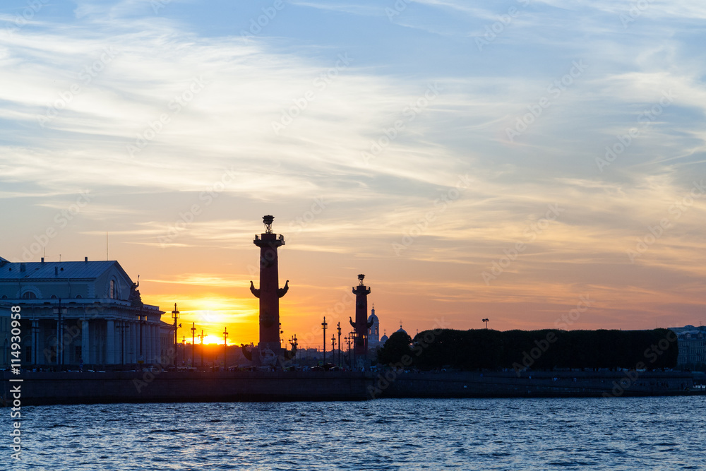Rostral column and arrow of Vasilyevsky Island under the bright sunset sky.