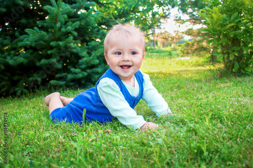Cute smiling little baby lying on a fresh green grass in a park.