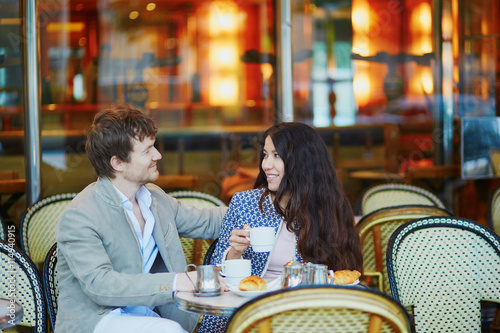 Couple drinking coffee and eating croissants in Parisian cafe