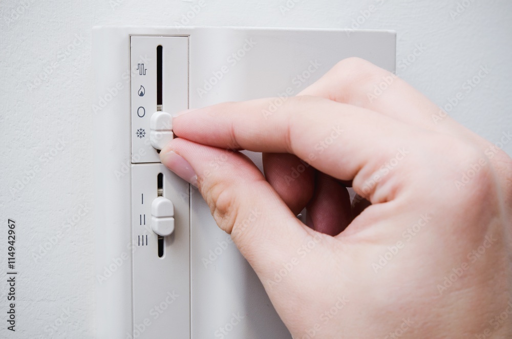 Hand switches air conditioner thermostat on wall
