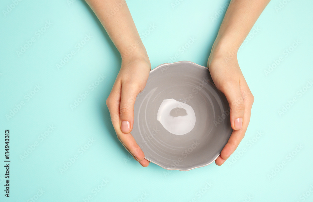 Female hands and empty bowl on turquoise background