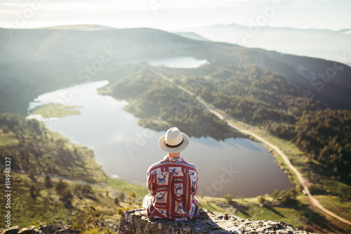 Man sitted in a rock looking at the lake in the mountains